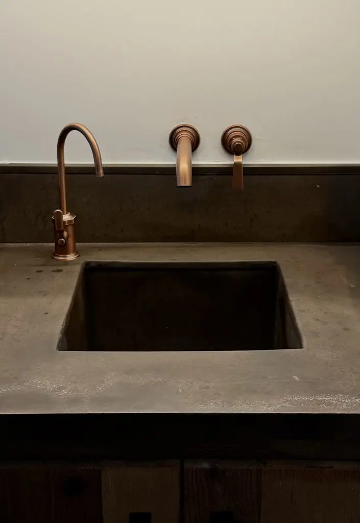 Copper faucet over concrete sink in bathroom.